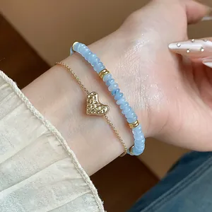 Gros plan d'un bracelet en perles d'aigue-marine et d'une fine chaîne dorée avec pendentif cœur
