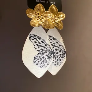 Close-up of golden metal flower earrings with butterfly wing printed acetate pendants