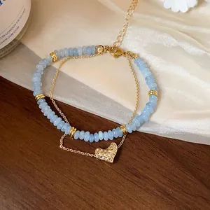 Gros plan d'un bracelet double rang avec perles bleues et pendentif cœur doré texturé