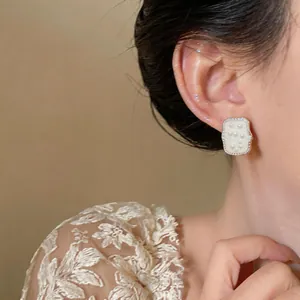 Close-up of French style square pearl stud earrings worn by a model with lace dress