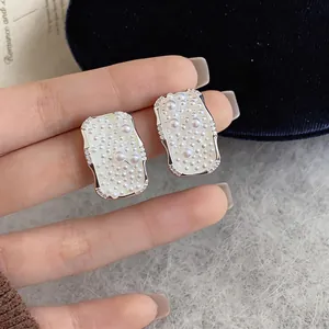 Detailed view of French square pearl stud earrings with silver needles on finger