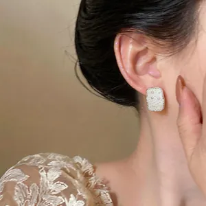 Detailed close-up of elegant square pearl stud earrings with rhinestone border on model ear