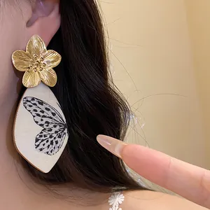 Close-up detail of vintage style large gold flower and butterfly print acetate drop earrings