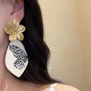 Macro view of elegant golden metal flower and butterfly print acetate drop earrings for women