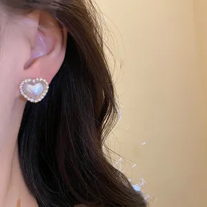 Detalle de pendiente de botón corazón de perla con borde de diamantes de imitación
