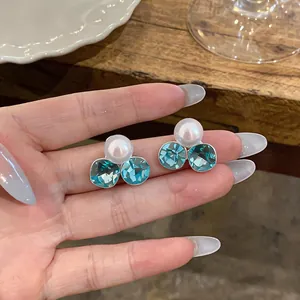 Detailed close-up view showing elegant blue rhinestone and pearl ear clips held on fingers