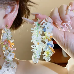 Dettaglio di orecchini pendenti con perline, fiori di vetro e farfalle fatti a mano