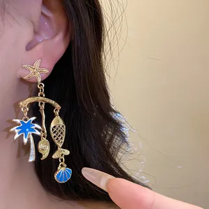 Close-up view of gold ocean-themed dangle earrings with starfish, palm tree, and shell charms