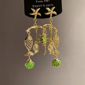 Close-up of gold starfish and shell earrings with green enamel coconut tree detail