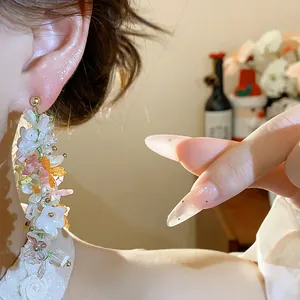Dettaglio di orecchini pendenti con fiori di vetro colorati e perle indossati sull'orecchio