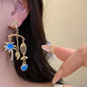 Close-up of gold ocean theme earrings with starfish, fish, and blue palm tree charms