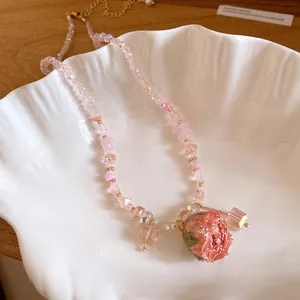 Close-up of elegant pink rose pendant and crystal beaded necklace on a white shell dish.