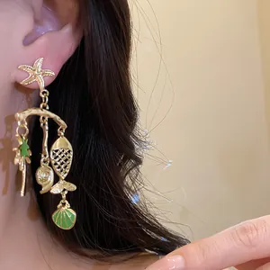 Close-up of vacation style gold earrings with starfish and green shell charms on ear.