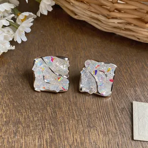 Close-up of square stud earrings with colorful crushed stone inlay and silver finish
