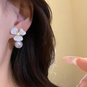 Detail of elegant white flower earring with sparkling center and hanging pearl decoration.