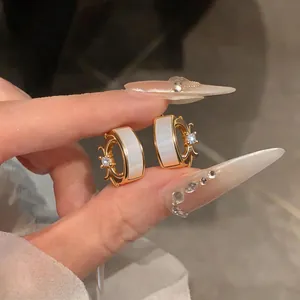 Detailed macro view of gold C-shaped earrings with mother-of-pearl and zircon iris motif