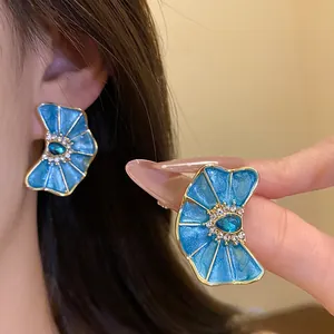 Vista detallada de pendientes de flor en esmalte azul con cristales brillantes.