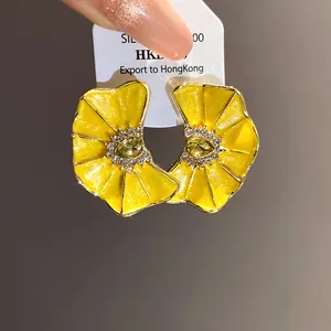Primer plano detallado de pendientes de flores amarillas plisadas con centros de cristal