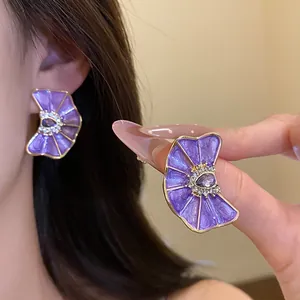 Detalle de pendientes de botón con forma de abanico en esmalte púrpura y detalles de cristal