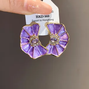 Detalle de pendientes de flores plisadas de color púrpura con cristales y baño de oro