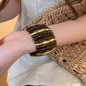 Dettaglio di un bracciale in acrilico marmorizzato e metallo dorato intrecciato sul polso
