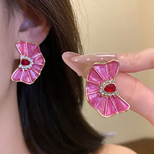 Detalle de pendientes flor rosa plisada con cristal rojo y borde dorado, estilo de lujo