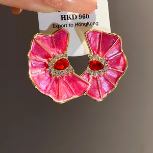 Detalle de pendientes de flor en esmalte rosa plisado con un centro de strass rojo brillante
