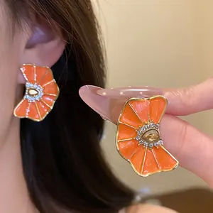 Primer plano de elegantes pendientes de flores plisadas naranjas con strass y oro