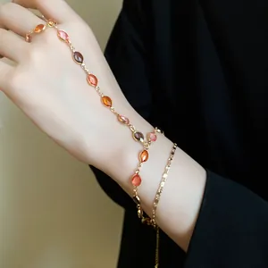 Dettaglio ravvicinato di bracciale a catena dorata con perle ovali in resina colorata.