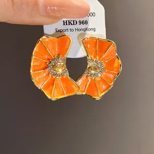 Detalle macro de pendientes de botón de flores plisadas naranjas con centro de strass