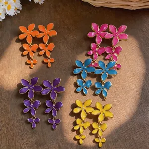Multiple pairs of colorful enamel flower tassel earrings on wood surface with sunlight shadows