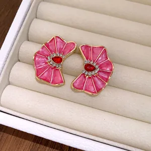 Detalle de pendientes de flores plisadas rosa con cristal rojo y strass