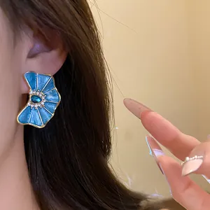 Primer plano de pendientes de flor de esmalte azul con pedrería en la oreja.