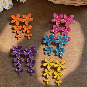 Vibrant enamel flower tassel earrings in multiple colors on a rustic wooden surface