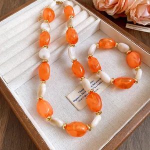 Close-up of elegant orange and white acrylic oval beaded necklace and bracelet set.