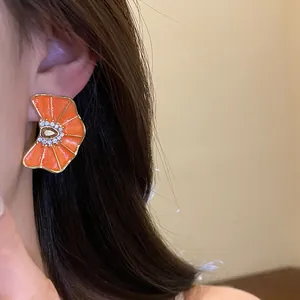 Primer plano de pendientes de flores de esmalte naranja con centro de diamantes de imitación