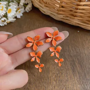 Detailed close-up showing the vibrant orange enamel finish of these triple flower tassel earrings