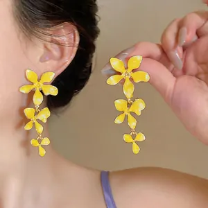 Close-up of vibrant yellow enamel flower tassel earrings featuring a delicate layered design.