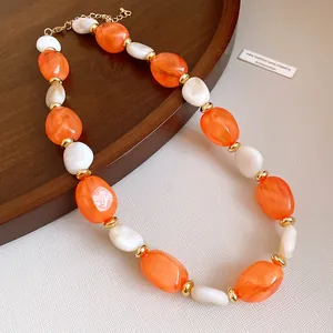 Macro view of chunky orange and white acrylic bead necklace with gold spacers