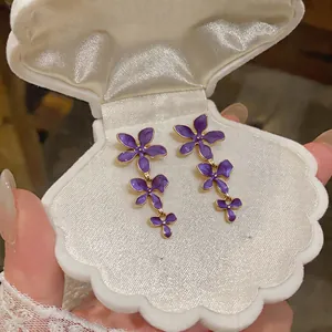 Purple enamel flower tassel drop earrings presented in a white shell-shaped jewelry box
