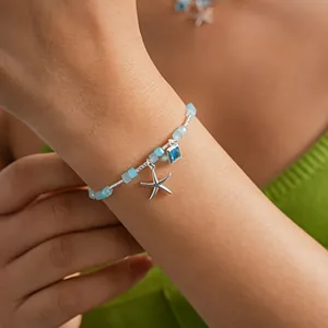 Gros plan d'un bracelet étoile de mer en argent avec perles de verre bleues au poignet.