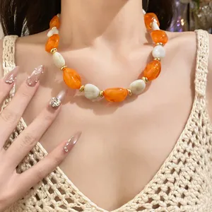 Close-up detail of an elegant orange and white acrylic oval beaded necklace on a model