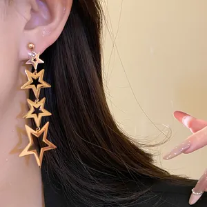 Close-up of gold-plated stainless steel star tassel earrings worn on a model's ear.
