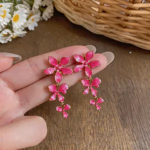Detailed close-up view of pink enamel triple flower tassel drop earrings held by hand