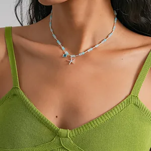 Détail d'un pendentif étoile de mer sur un collier de perles bleues et blanches et haut vert