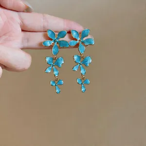 Detail view of elegant light blue enamel flower tassel earrings with golden metal edges.