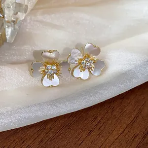 Détail macro de boucles d'oreilles fleurs plaquées or 14 carats avec zircon et nacre.