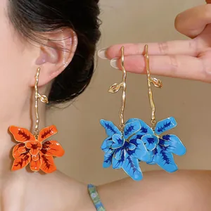 Close-up of vibrant orange and blue enamel flower drop earrings with golden stems