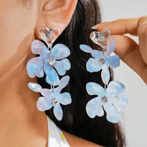 Dettaglio di orecchini a fiore in resina blu con perno a cuore e strass luminosi