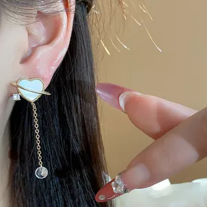 Vue détaillée d'une boucle d'oreille cœur planète dorée 14k avec chaîne en zircon